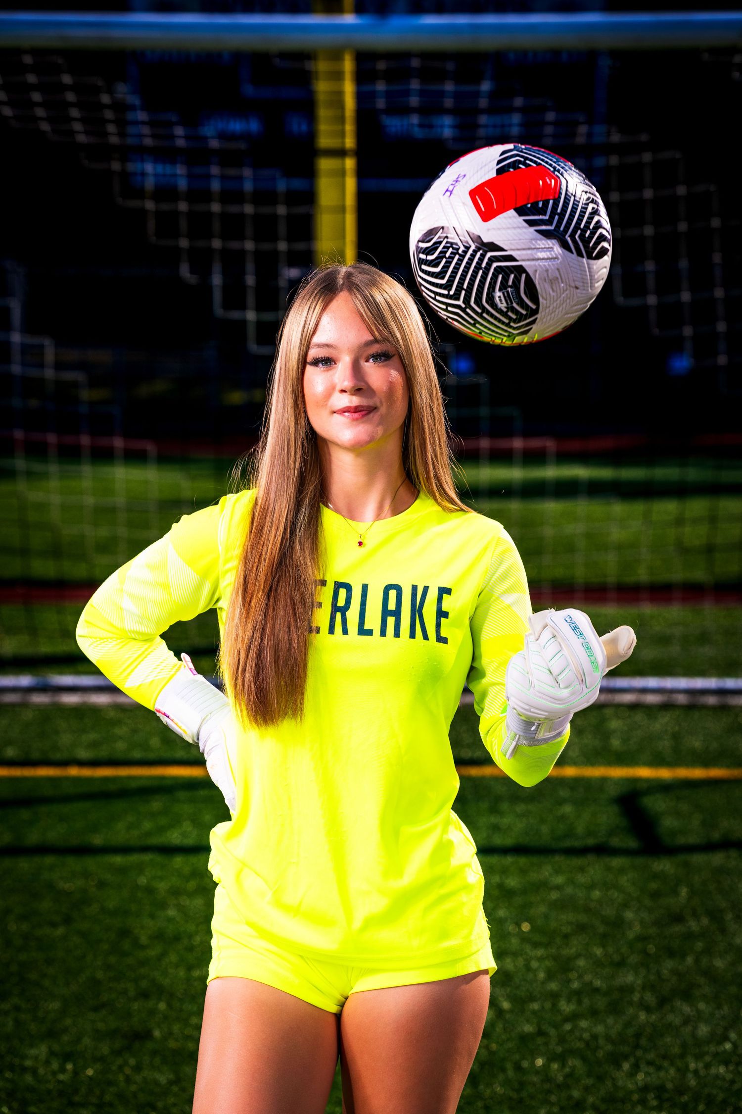 Soccer goalkeeper in bright yellow uniform poses with ball against dark background.