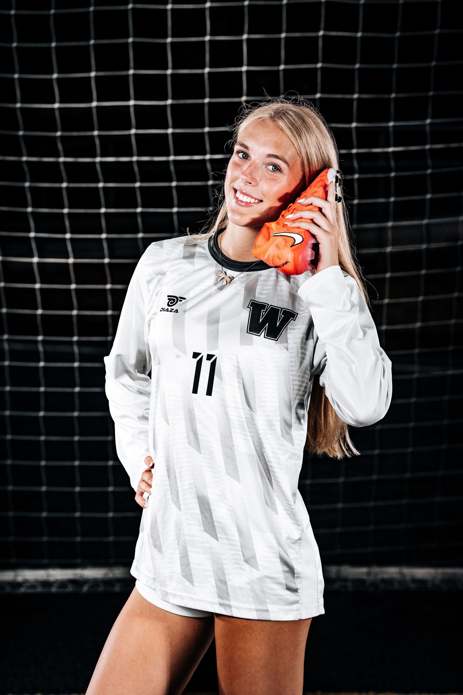 Soccer player in white jersey number 11 poses with orange ball against goal net.