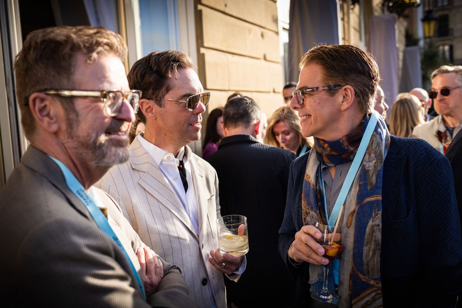 Three men conversing and holding drinks at an elegant outdoor networking cocktail reception.