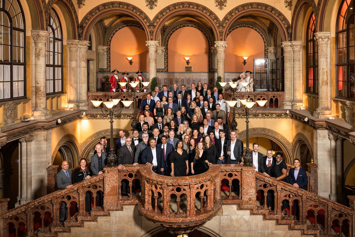 Large group photo of professionals posing on an ornate staircase in a historic European building.