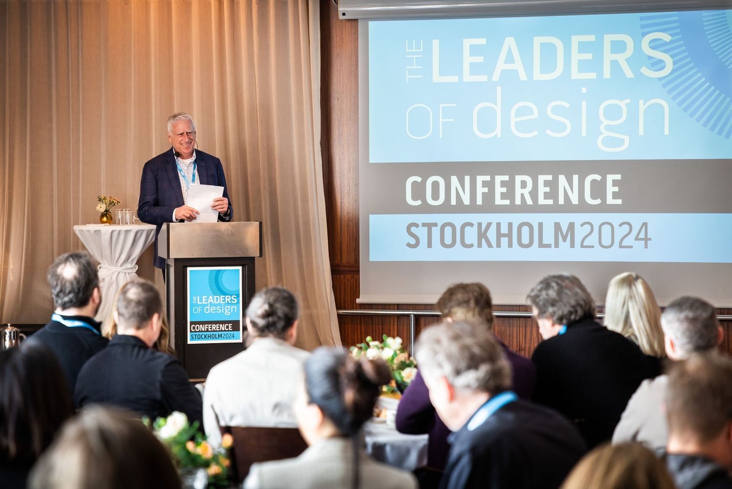 Speaker presenting at Leaders of Design Conference Stockholm 2024 podium before seated audience.