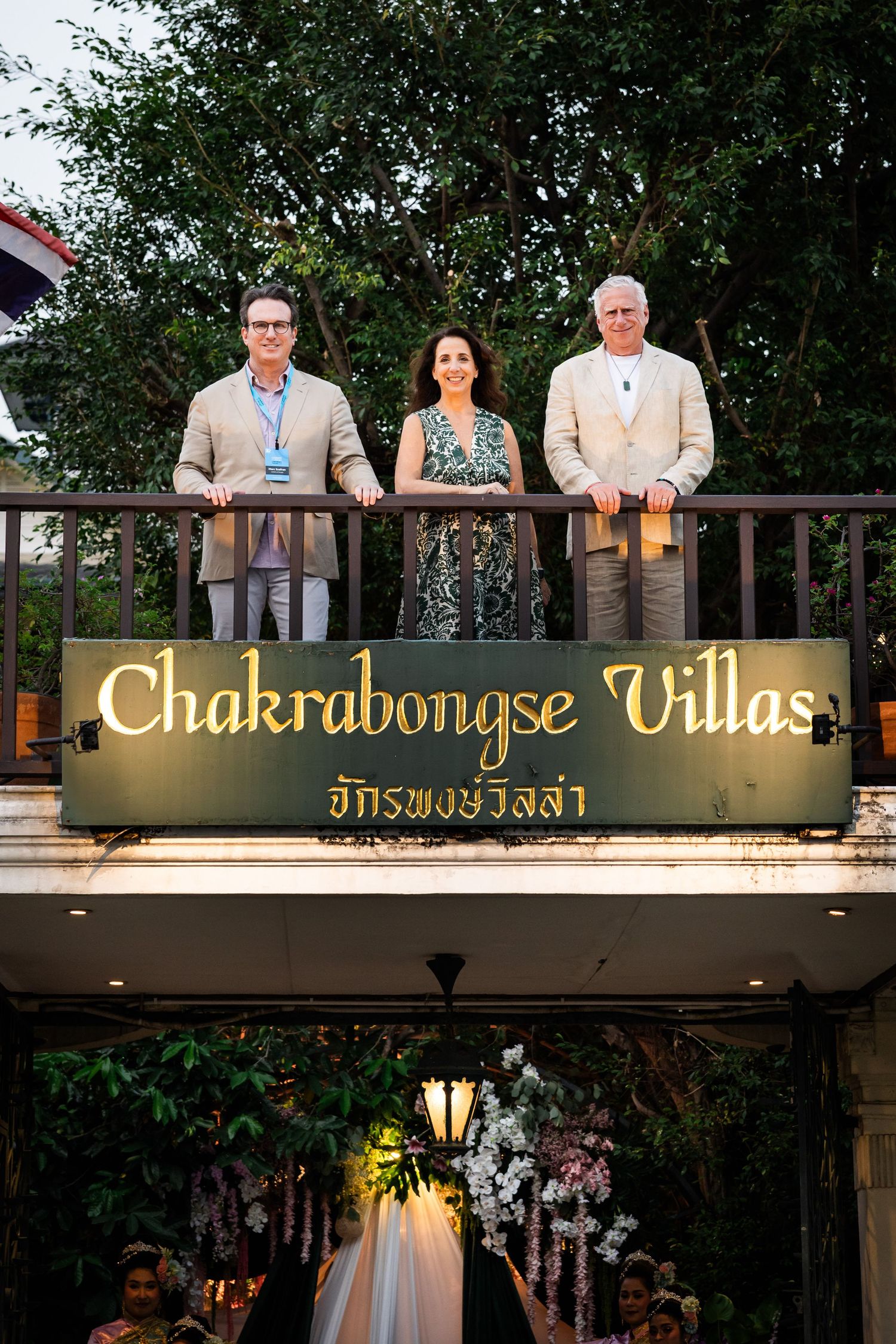 Three event organizers posing on balcony above Chakrabongse Villas sign in Bangkok Thailand.