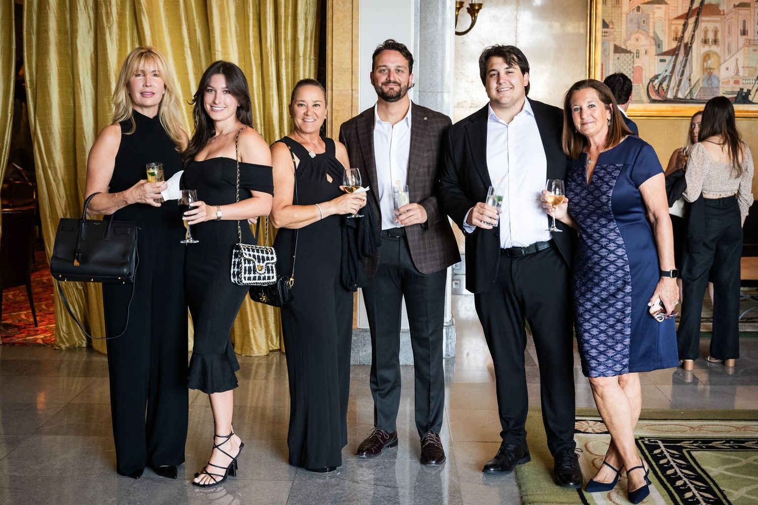 Group of six professionally dressed guests smiling and holding drinks at an elegant cocktail reception.