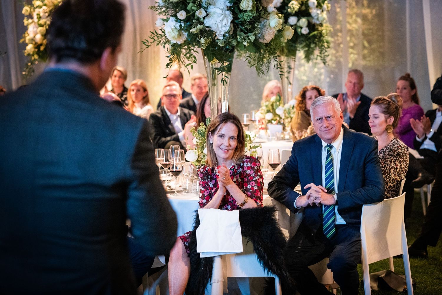 Guests seated at an elegant floral-decorated gala dinner event listening to a speaker.