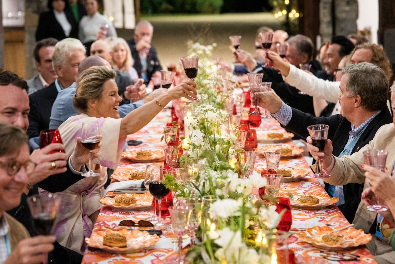 Guests raising wine glasses in a celebratory toast at a festive outdoor long table dinner party.