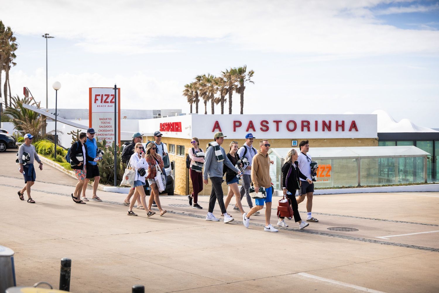 Group of tourists walking past A Pastorinha restaurant sign near a beachfront promenade with palm trees.