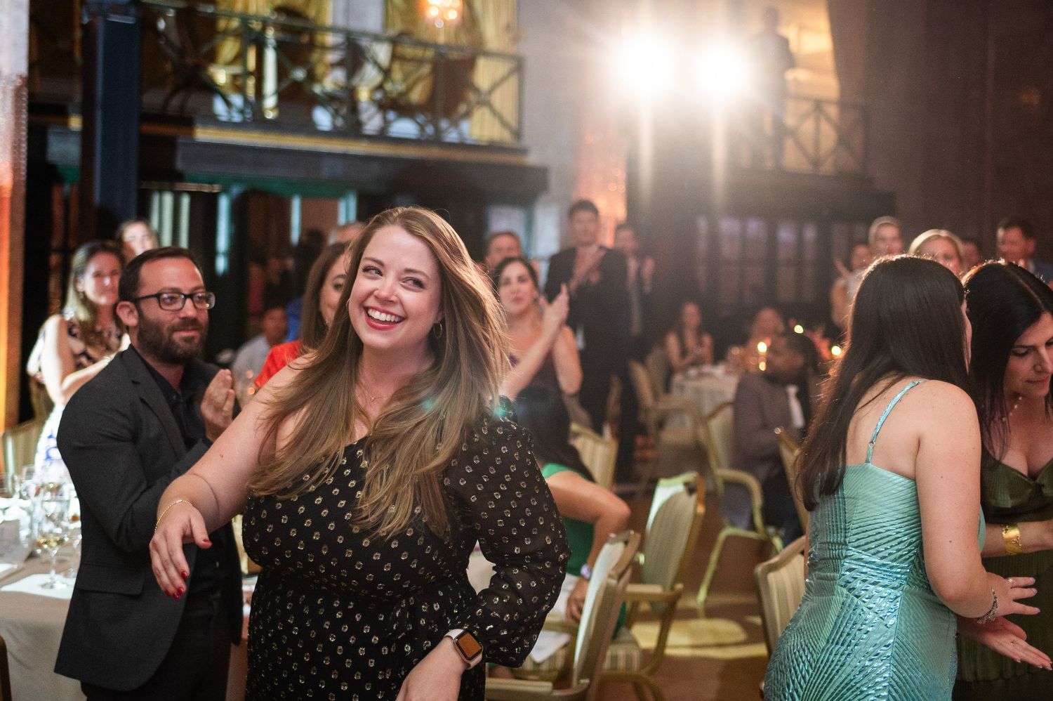 Woman in polka dot dress dancing and smiling at an elegant evening gala event.