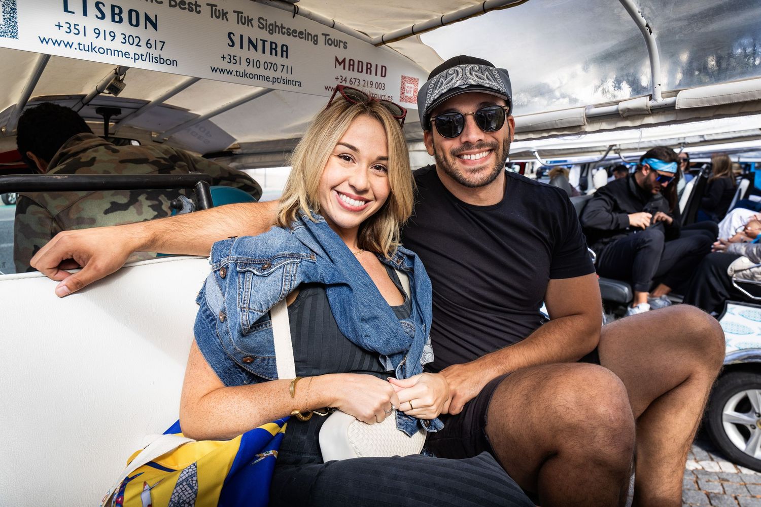 A smiling couple sits together on a tuk-tuk sightseeing tour vehicle in Lisbon, Portugal.