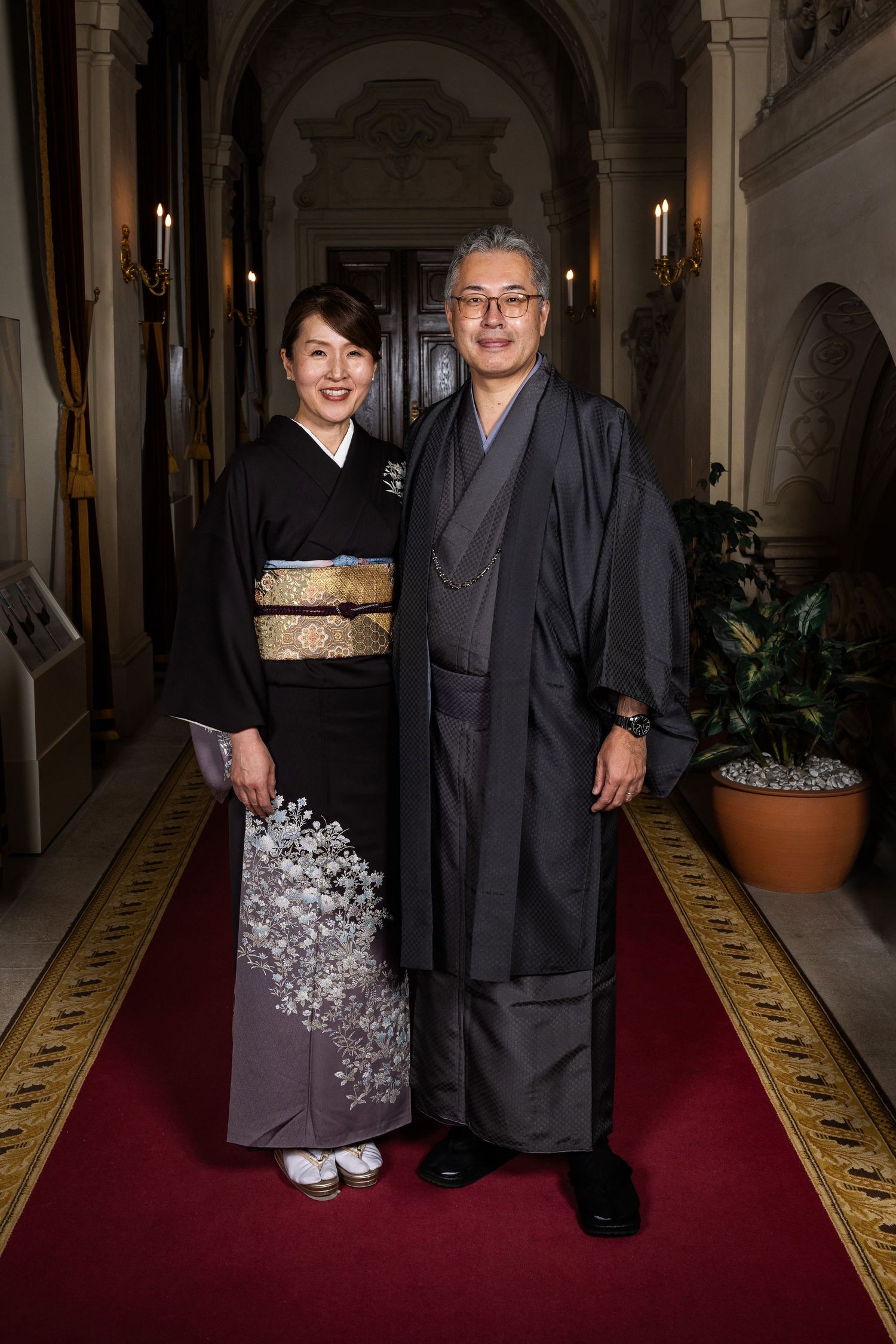 Japanese couple in traditional black kimono and hakama posing in an elegant European palace corridor.