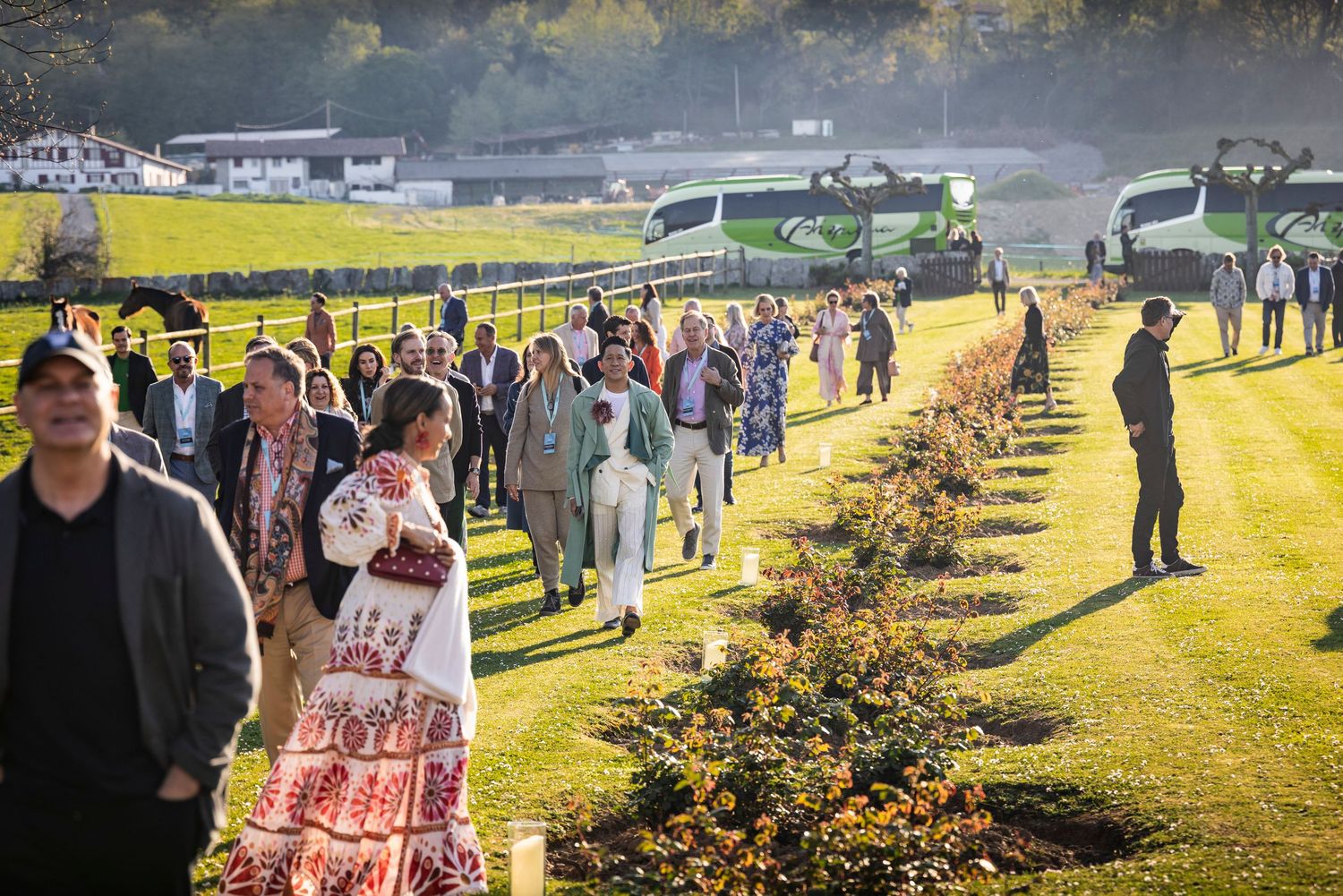 Large group of people walking along a sunny garden path lined with autumn trees and green coaches.