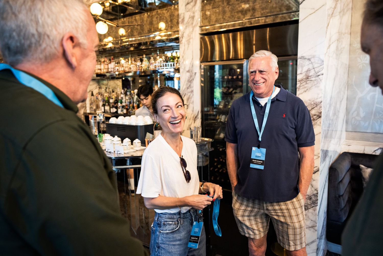 Three conference attendees laughing and socializing near a bar at a networking event.