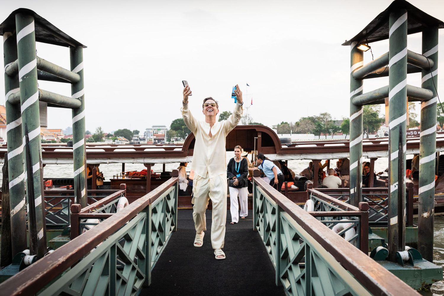 Person in white suit walking down a dock gangway with arms raised in celebration near a river.