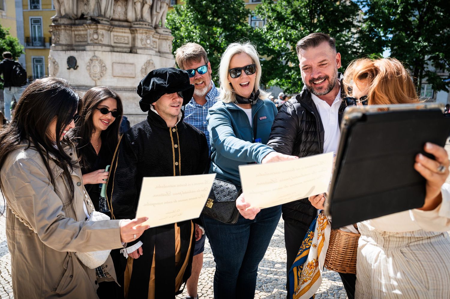 Tour group reviewing documents with a costumed guide near a historic fountain.