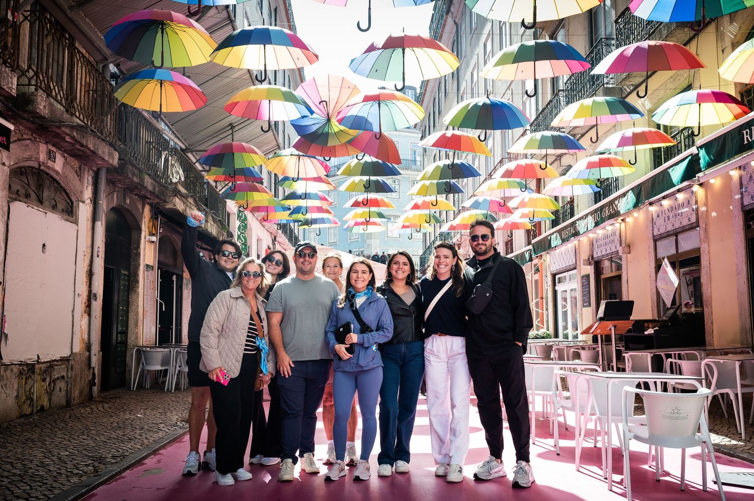 Group of friends posing under colorful umbrella street installation in a vibrant outdoor alley.