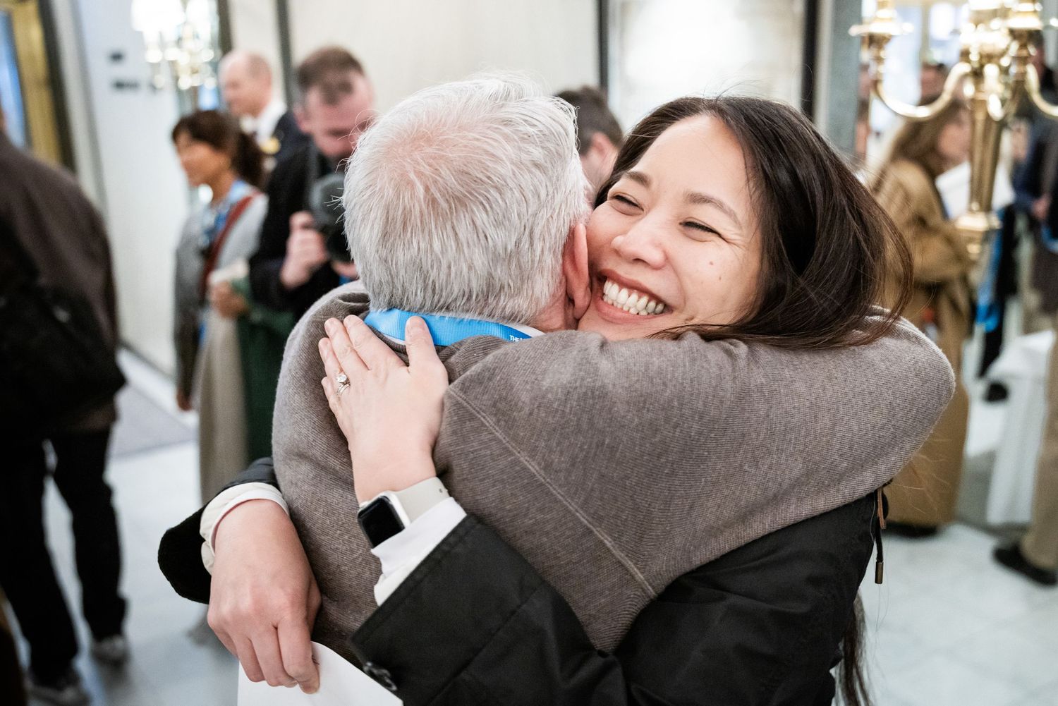 Joyful woman smiling broadly while sharing a warm hug with an older man at a social gathering.