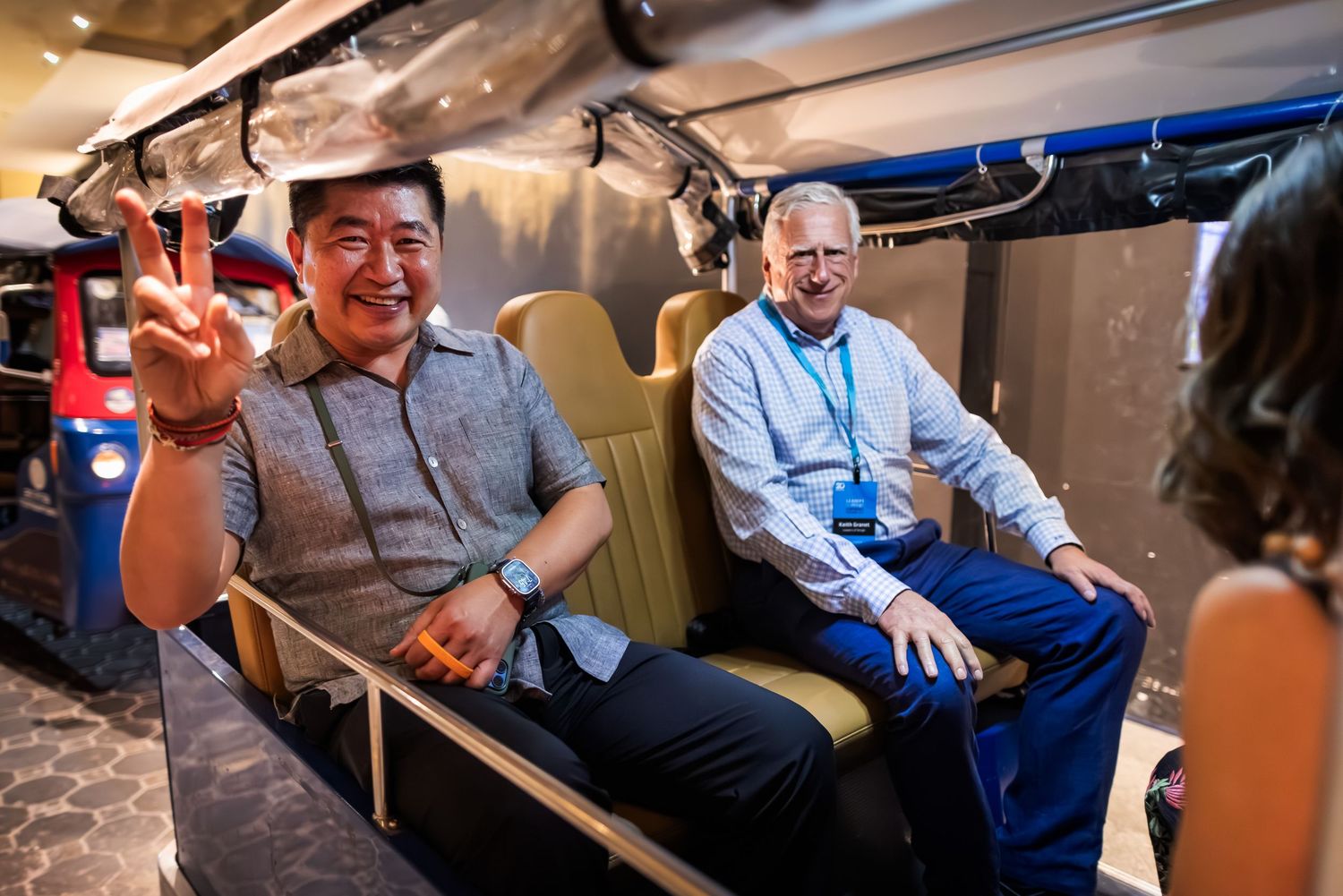Two men smiling and laughing while riding in a tuk-tuk vehicle during a city tour.