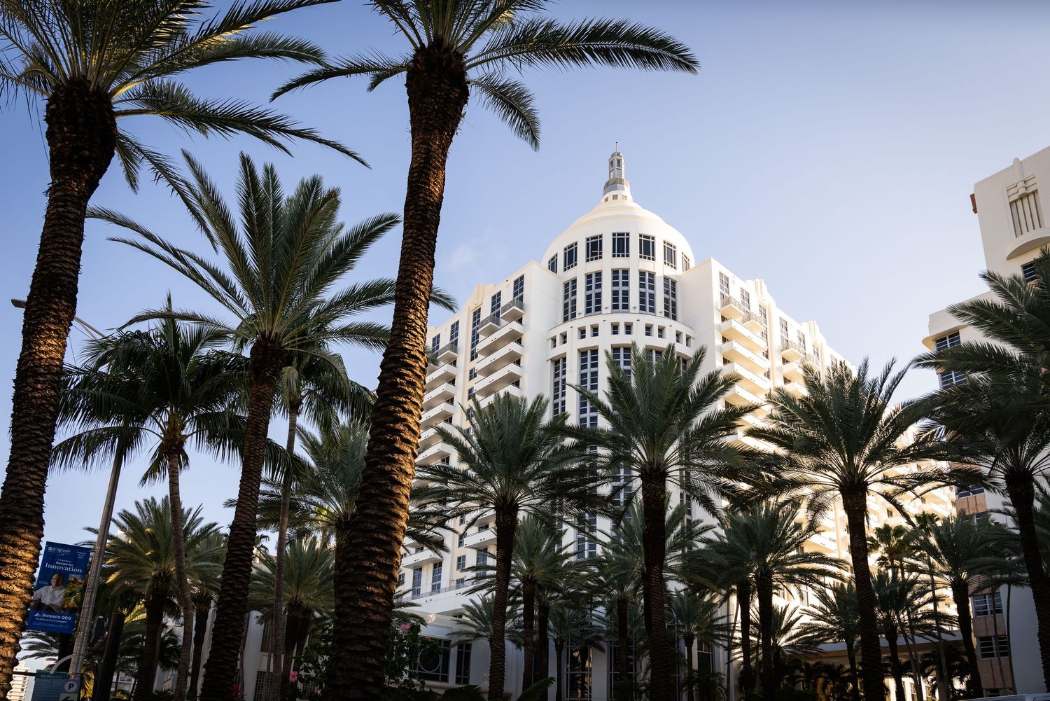Luxury white Art Deco hotel building surrounded by tall palm trees against a clear blue sky.