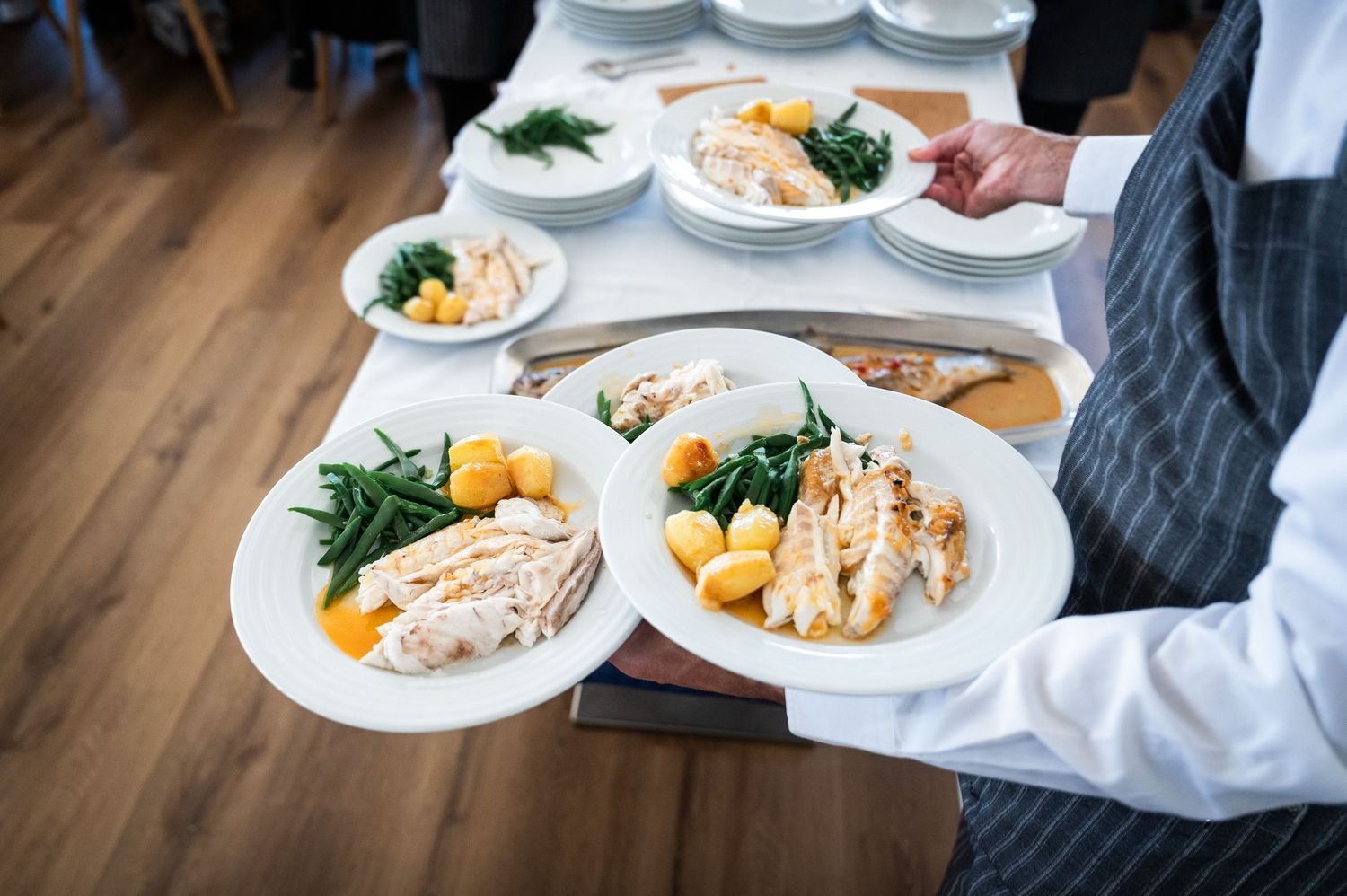 Waiter serving plates of grilled chicken with green beans and potatoes in a restaurant.