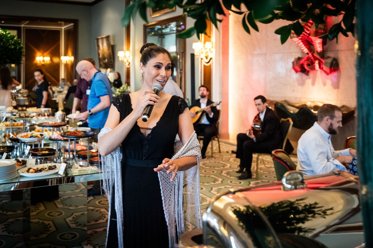 A woman in black speaks into a microphone at a sophisticated indoor catered event.