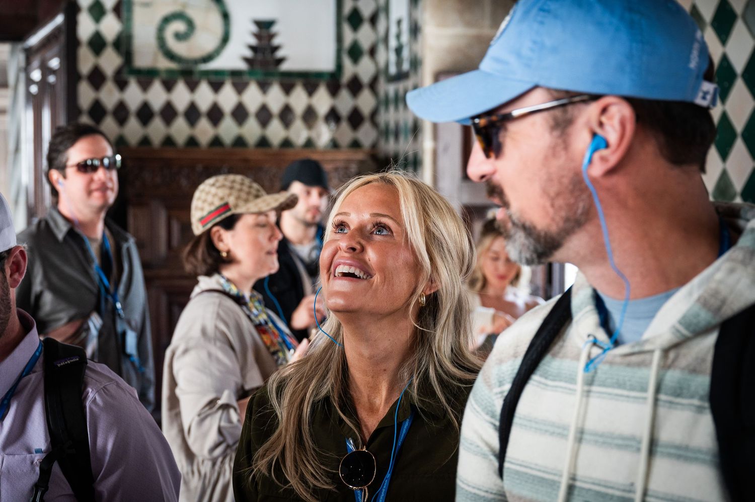 Excited tourists listening to a guide inside a historic ornate tiled building.