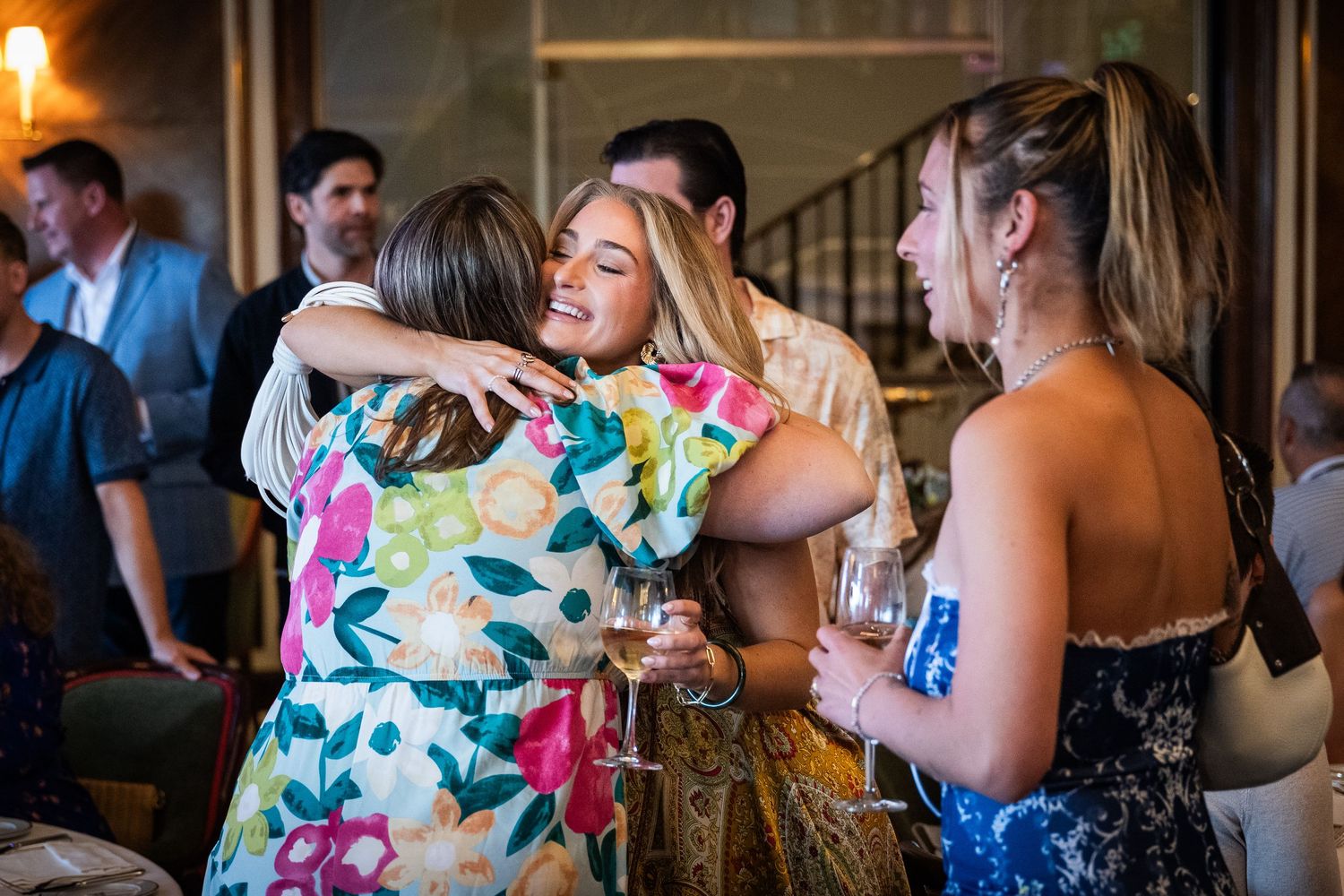 Guests share warm hugs and smiles at a lively indoor social gathering event.
