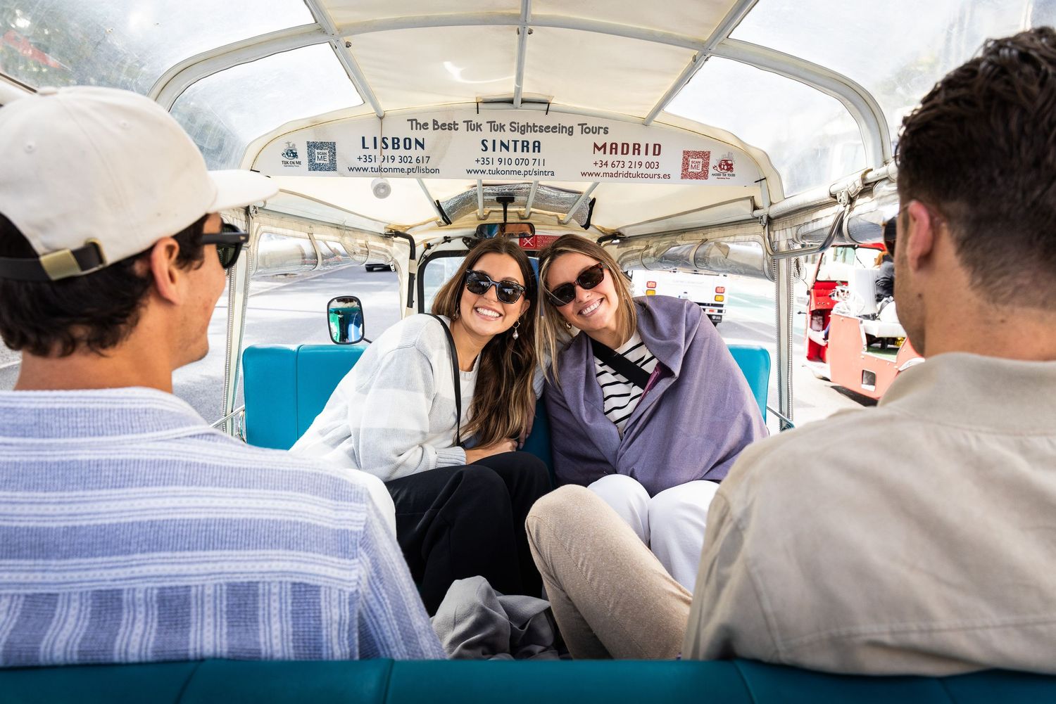 Two smiling women enjoy a tuk-tuk sightseeing tour, seated inside the open-air vehicle.
