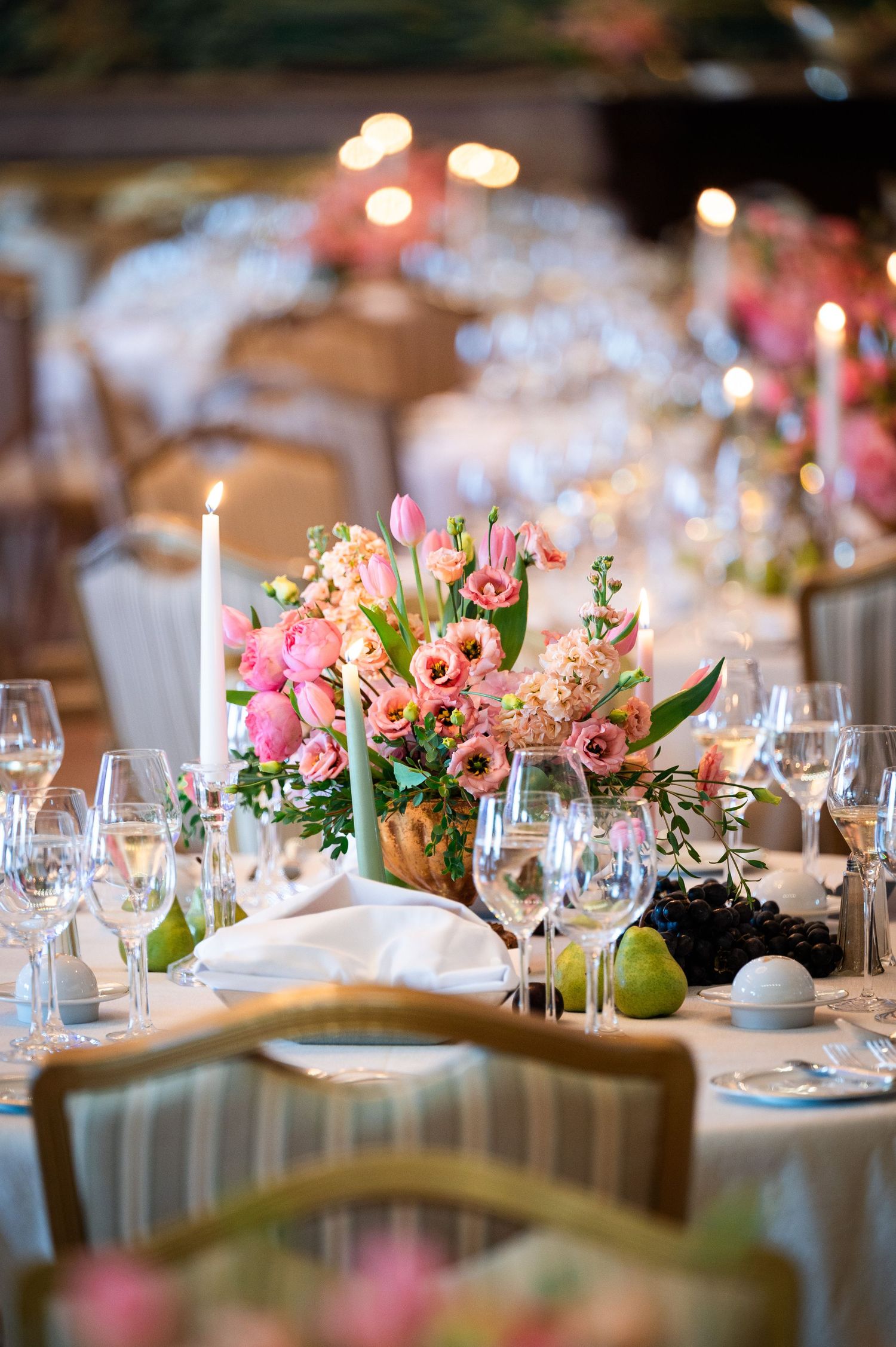 Elegant table setting with pink floral centerpiece, crystal wine glasses, candles, and fresh fruit.