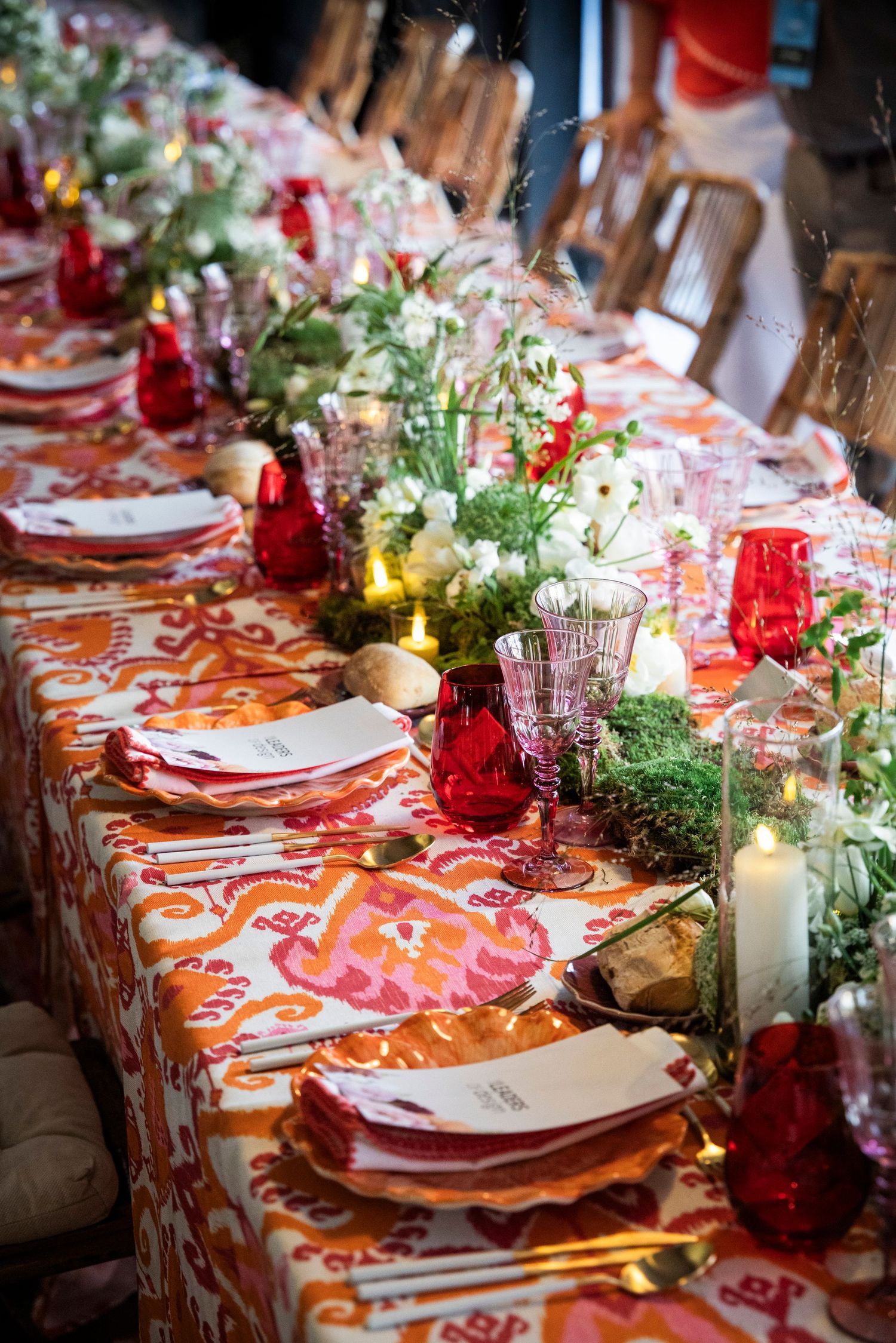 Elegantly decorated long dining table with red glassware, white flowers, and colorful ikat tablecloth.