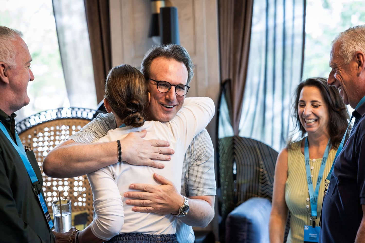 Professionals warmly embracing at a networking event while colleagues smile nearby.