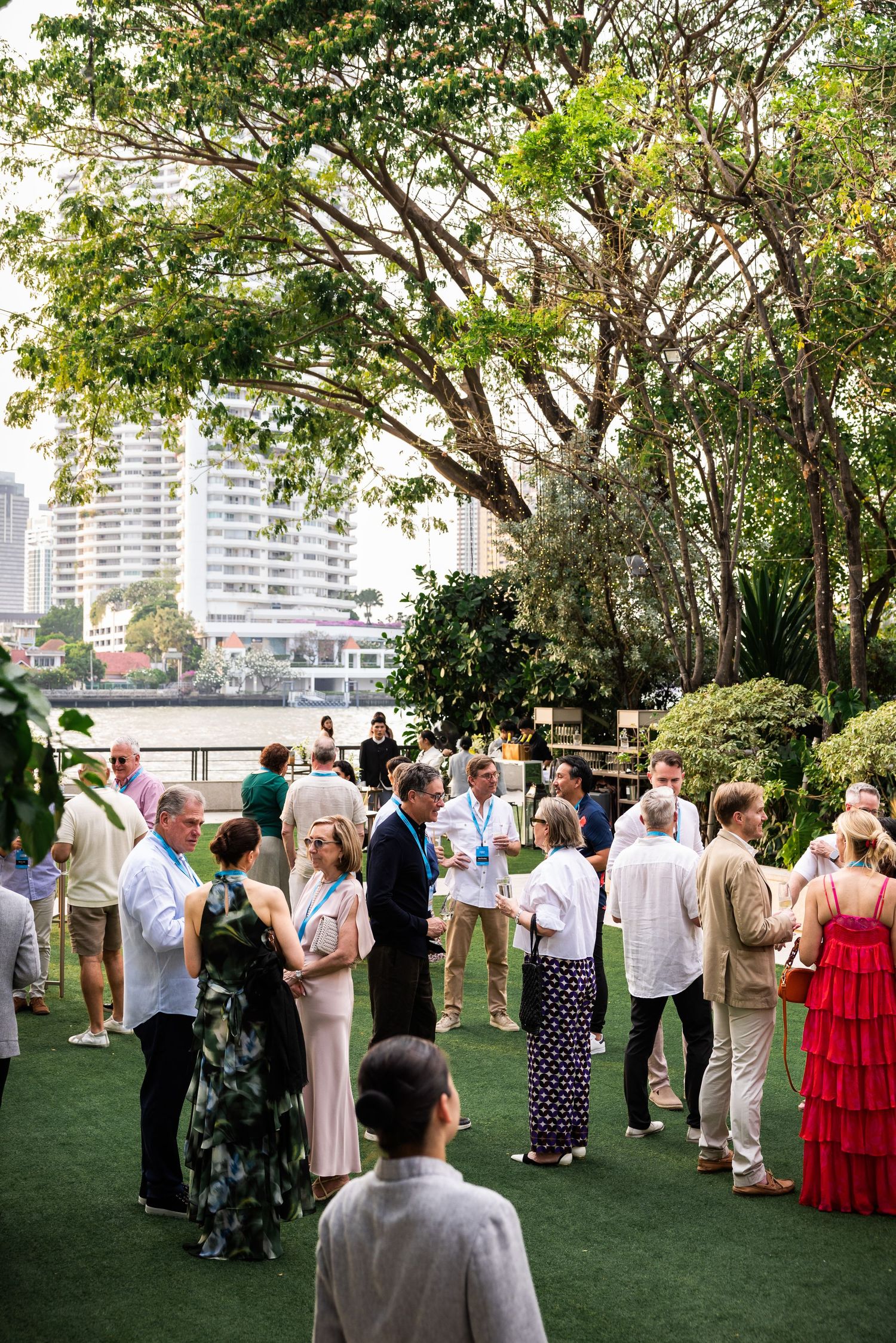 Conference attendees mingling outdoors near a river with city skyline in background.