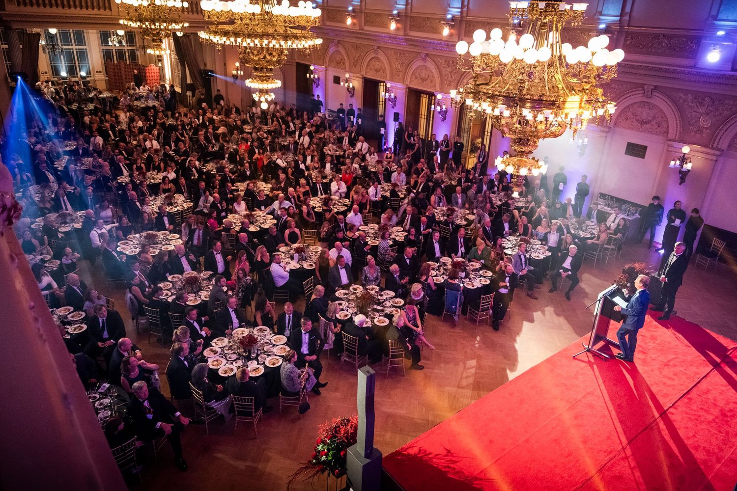 Aerial view of a grand ballroom filled with guests at round tables during a formal gala event.