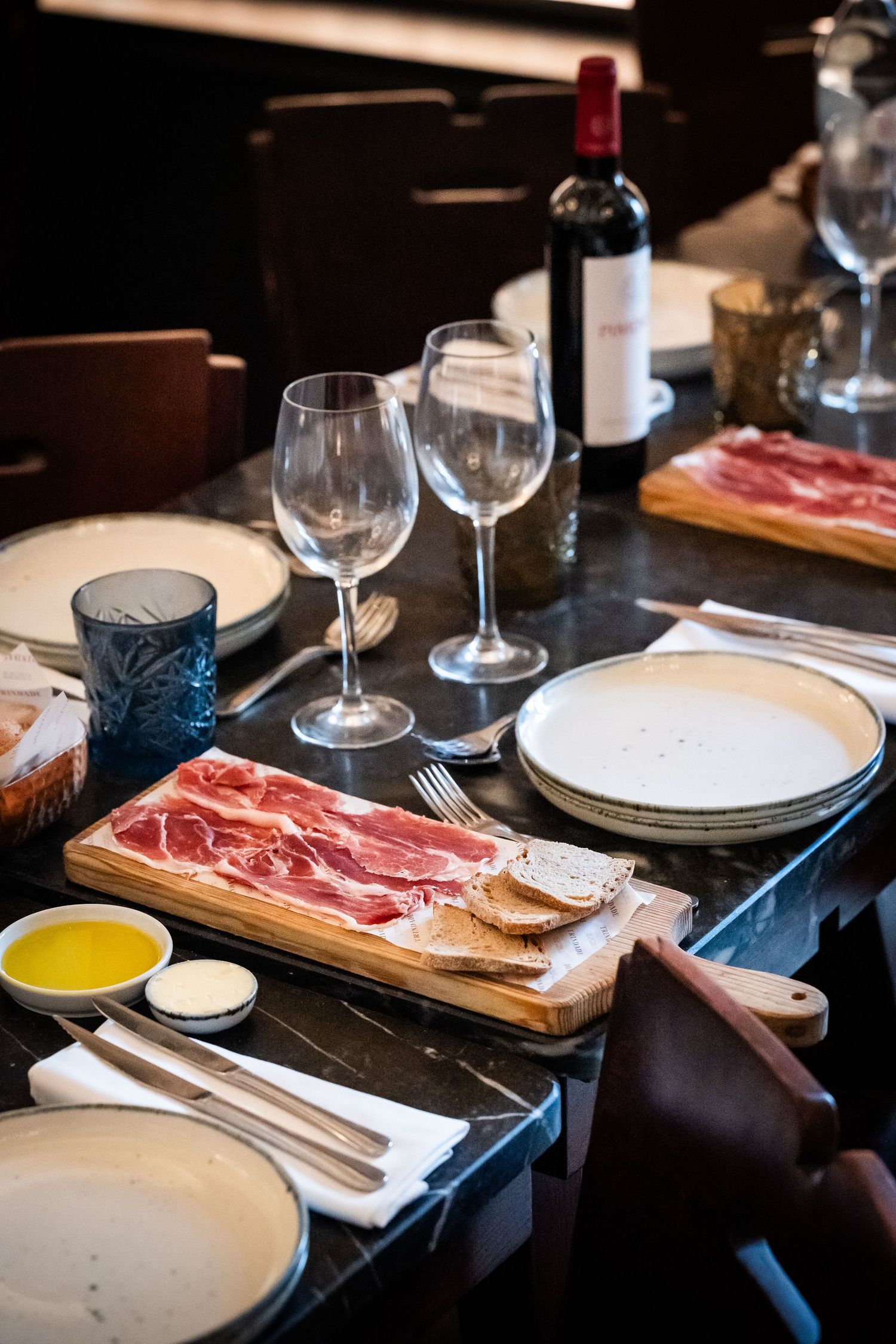 Elegant restaurant table set with charcuterie board, wine glasses, and red wine bottle.