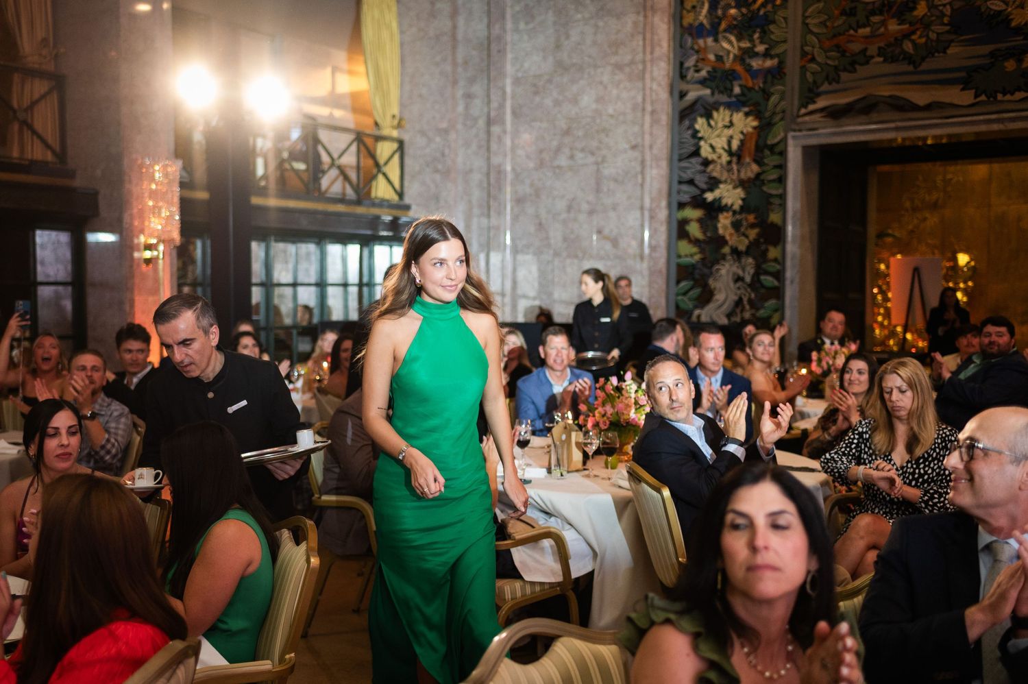 Woman in elegant green halter gown walking through a decorated banquet hall event.