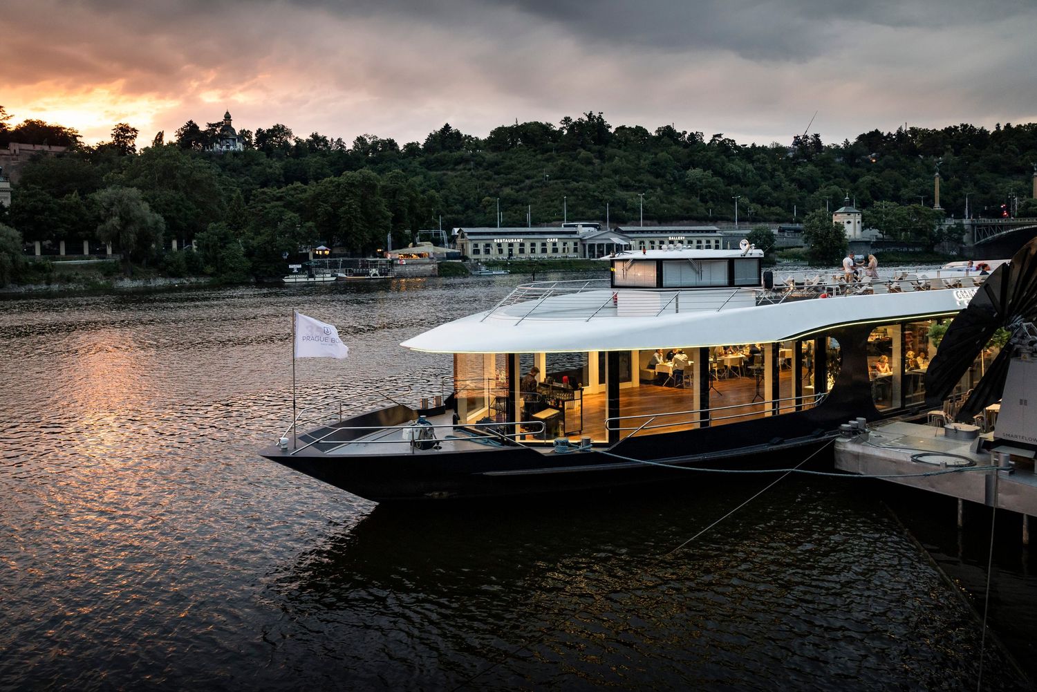 Elegant luxury boat moored on a calm river at sunset with glowing interior lights.