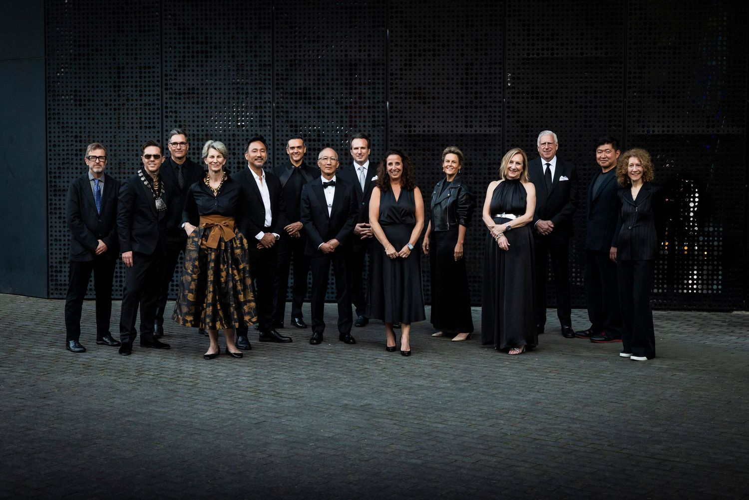 Group of fourteen formally dressed design conference delegates posing together for official group photo.