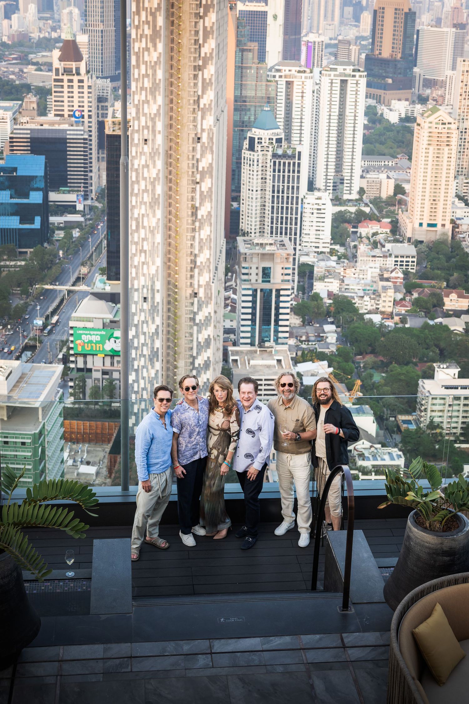 Group of six people posing together on a high-rise rooftop terrace with city skyline backdrop.