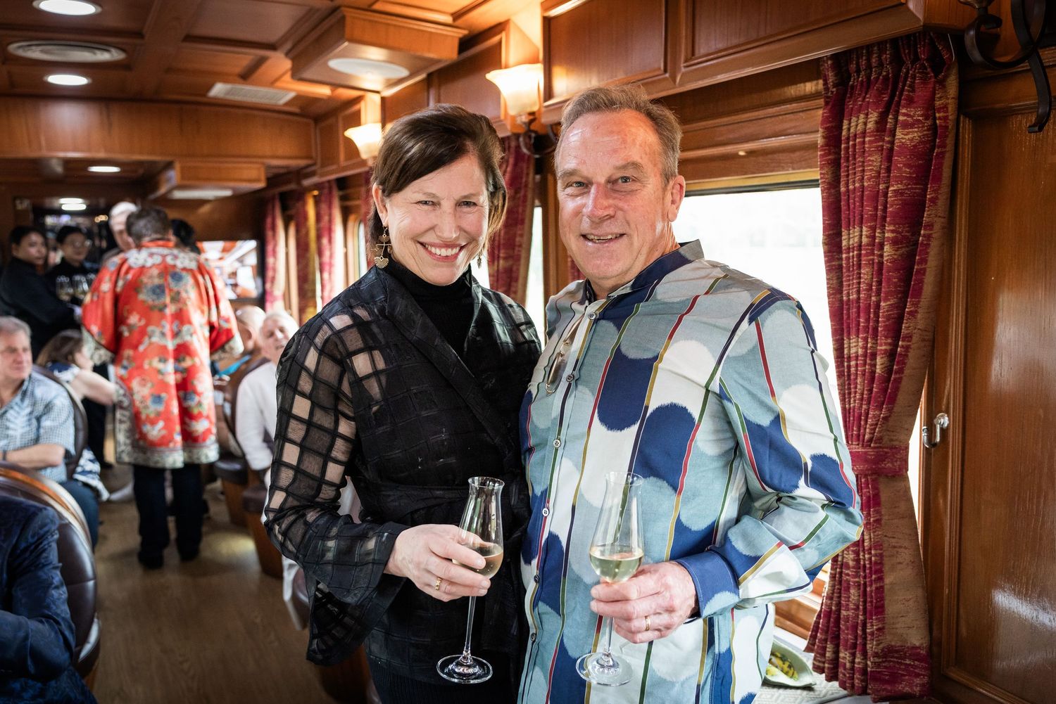 Smiling couple holding champagne glasses aboard a luxurious vintage train car.