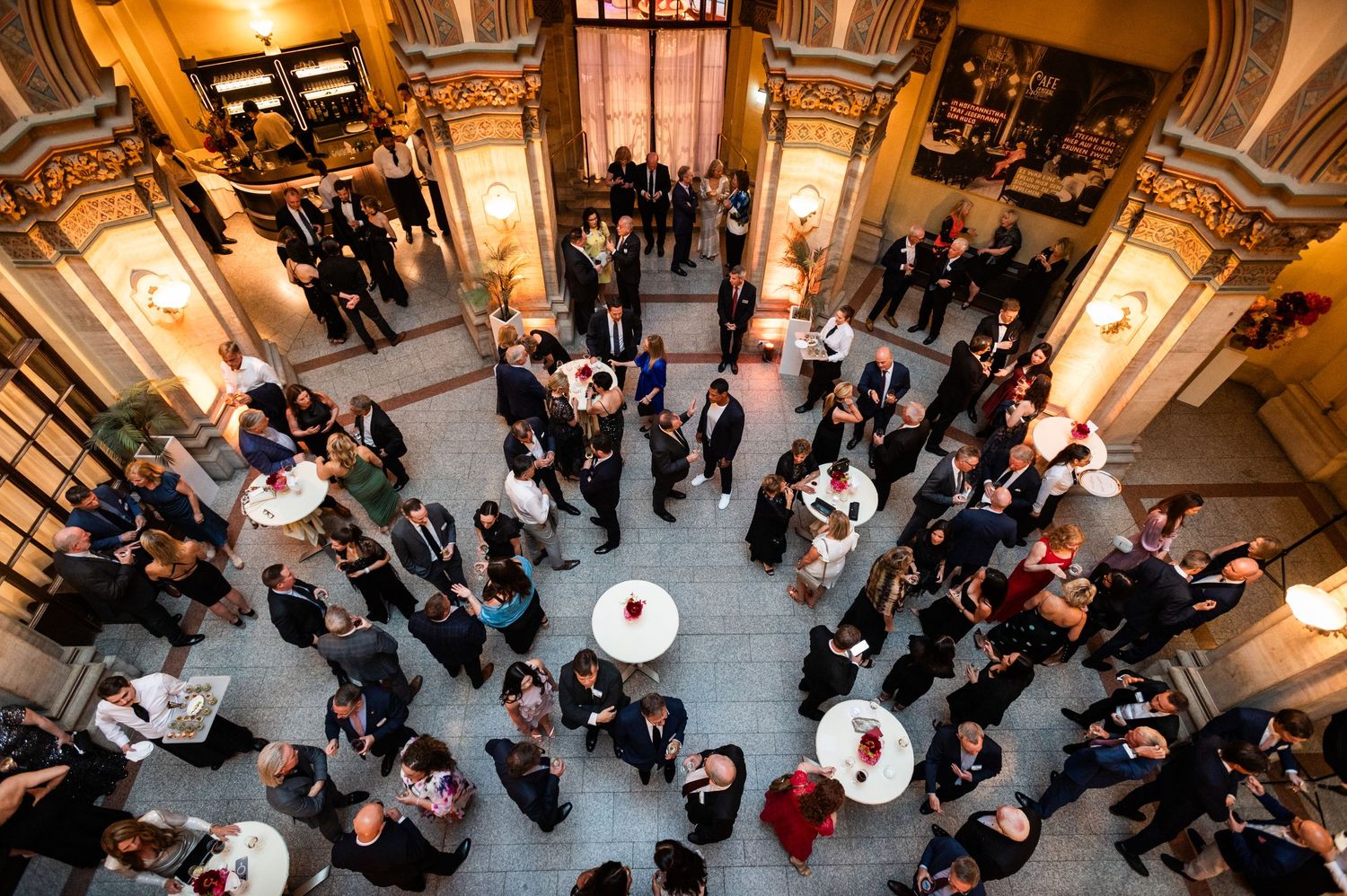 Aerial view of elegantly dressed guests mingling in an ornate historic venue lobby during a reception.