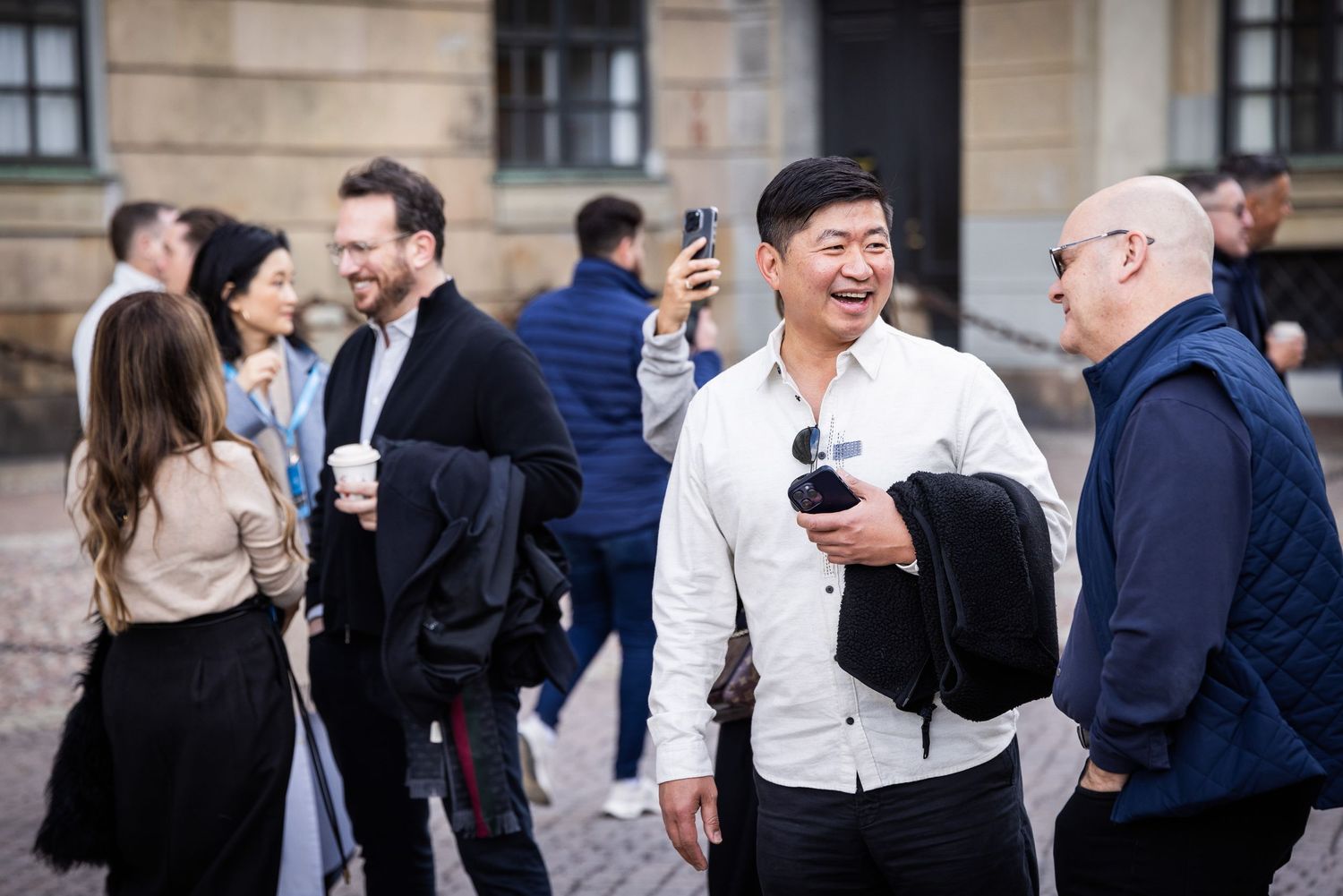 Group of professionals networking outdoors at a design conference in Stockholm, smiling and holding coffee.
