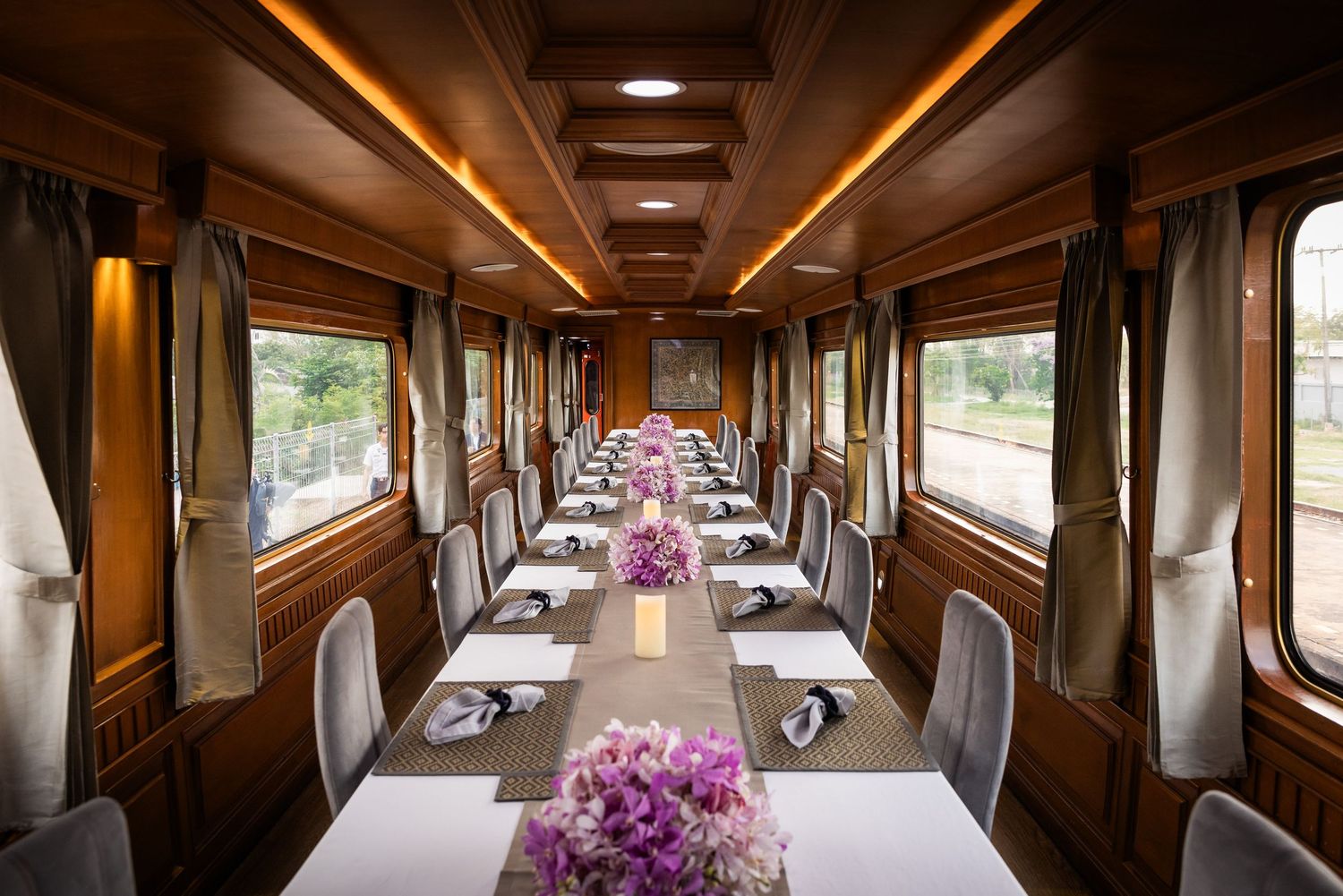 Elegant train dining car with long white-clothed tables adorned with purple floral centerpieces.