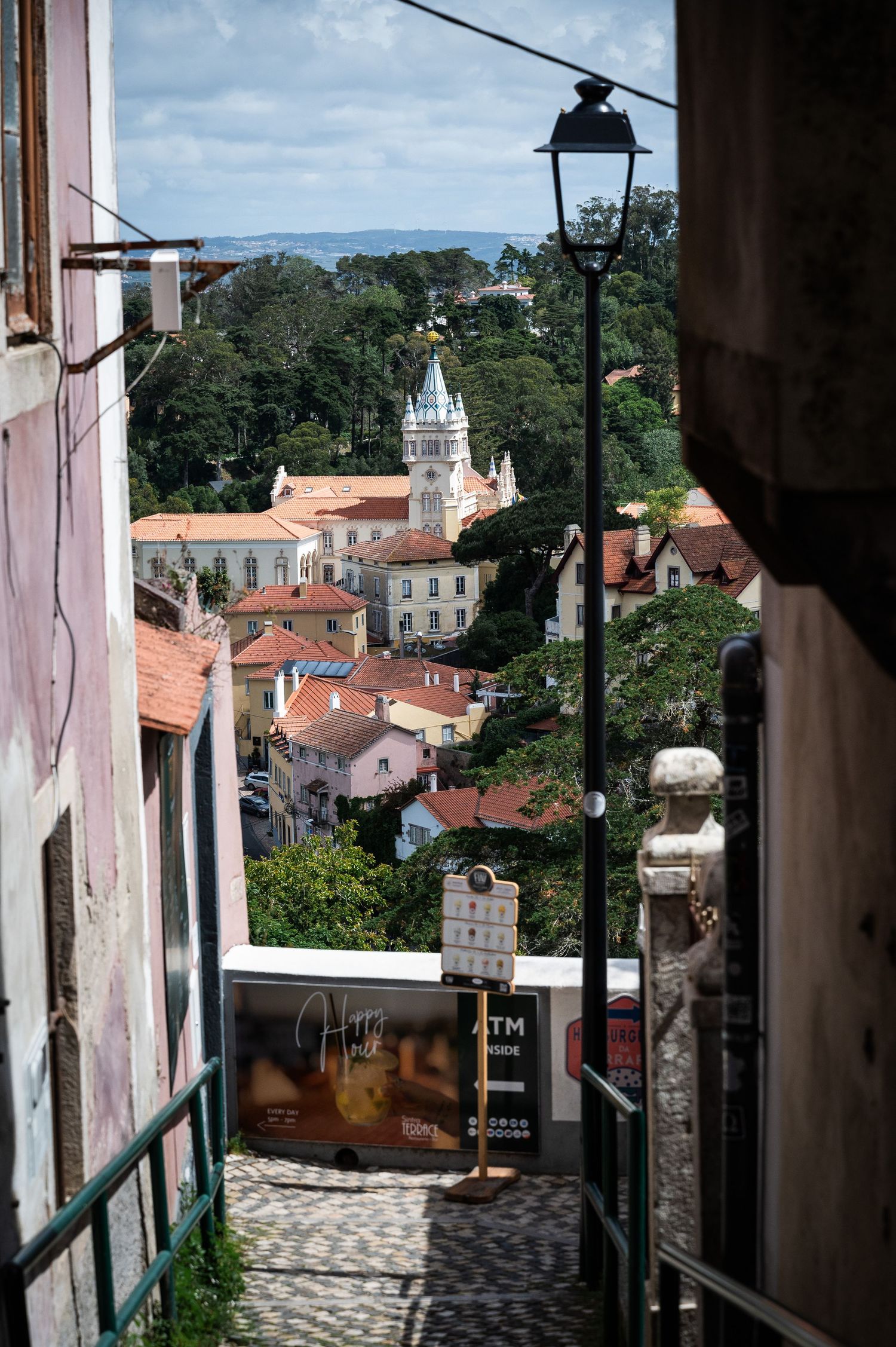 Narrow cobblestone alley in Sintra Portugal with view of historic town buildings and white clock tower.