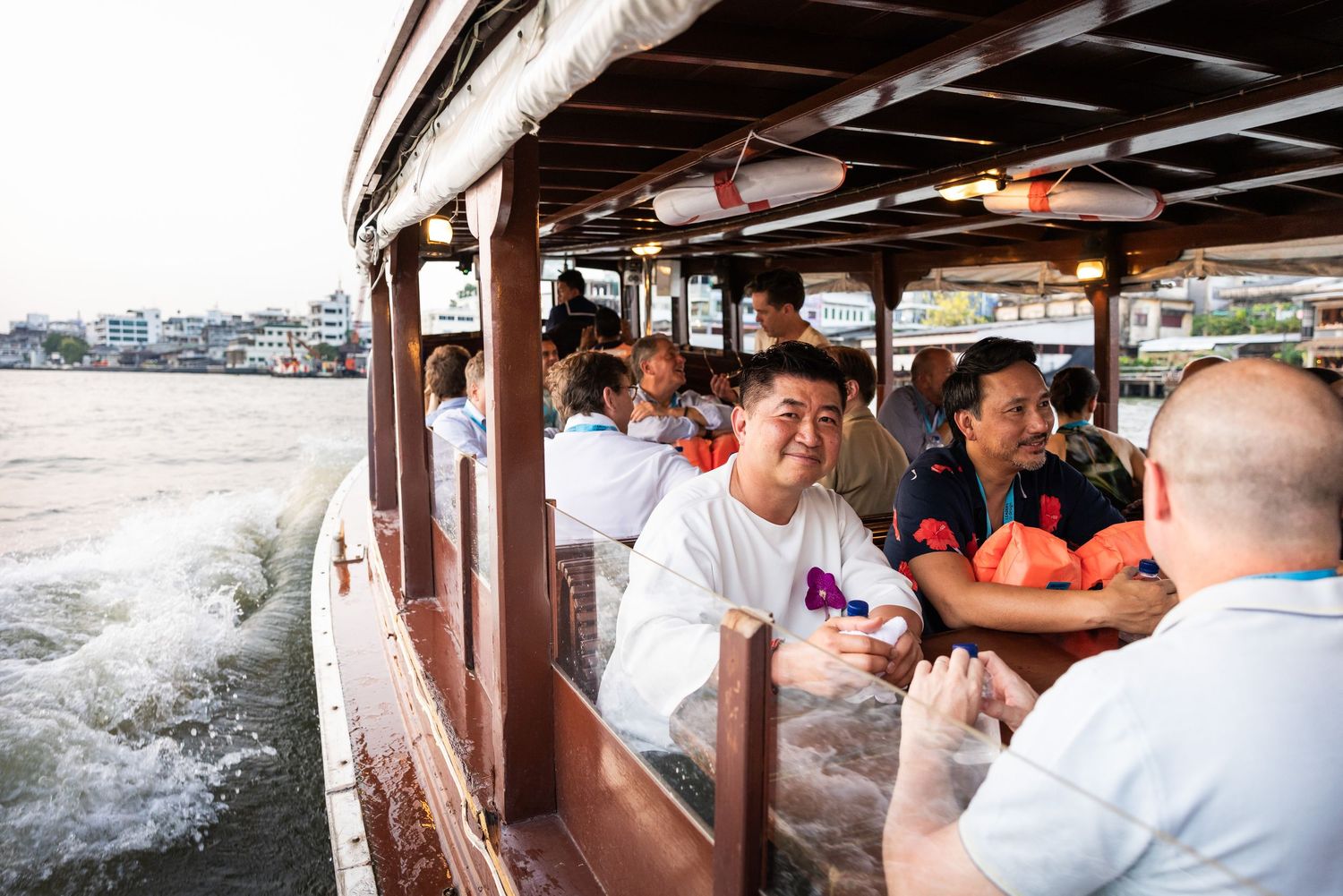 Happy conference attendees enjoying a scenic boat ride along Bangkok river at sunset.
