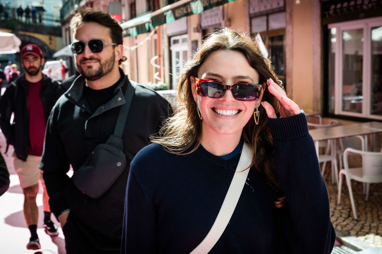 Smiling woman wearing sunglasses walking through a busy outdoor market street.