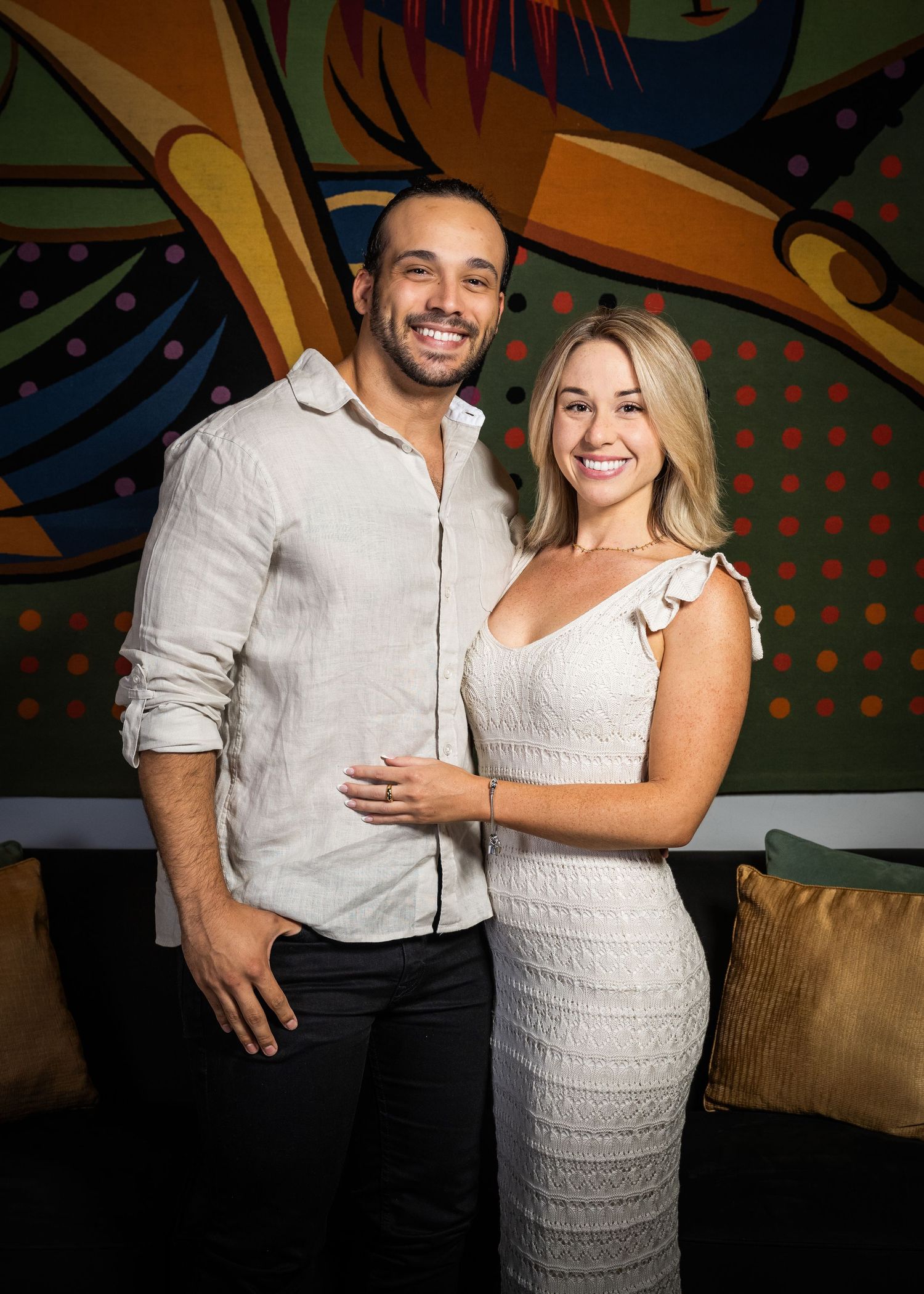 A stylish couple smiles warmly while posing together in front of a vibrant colorful mural.