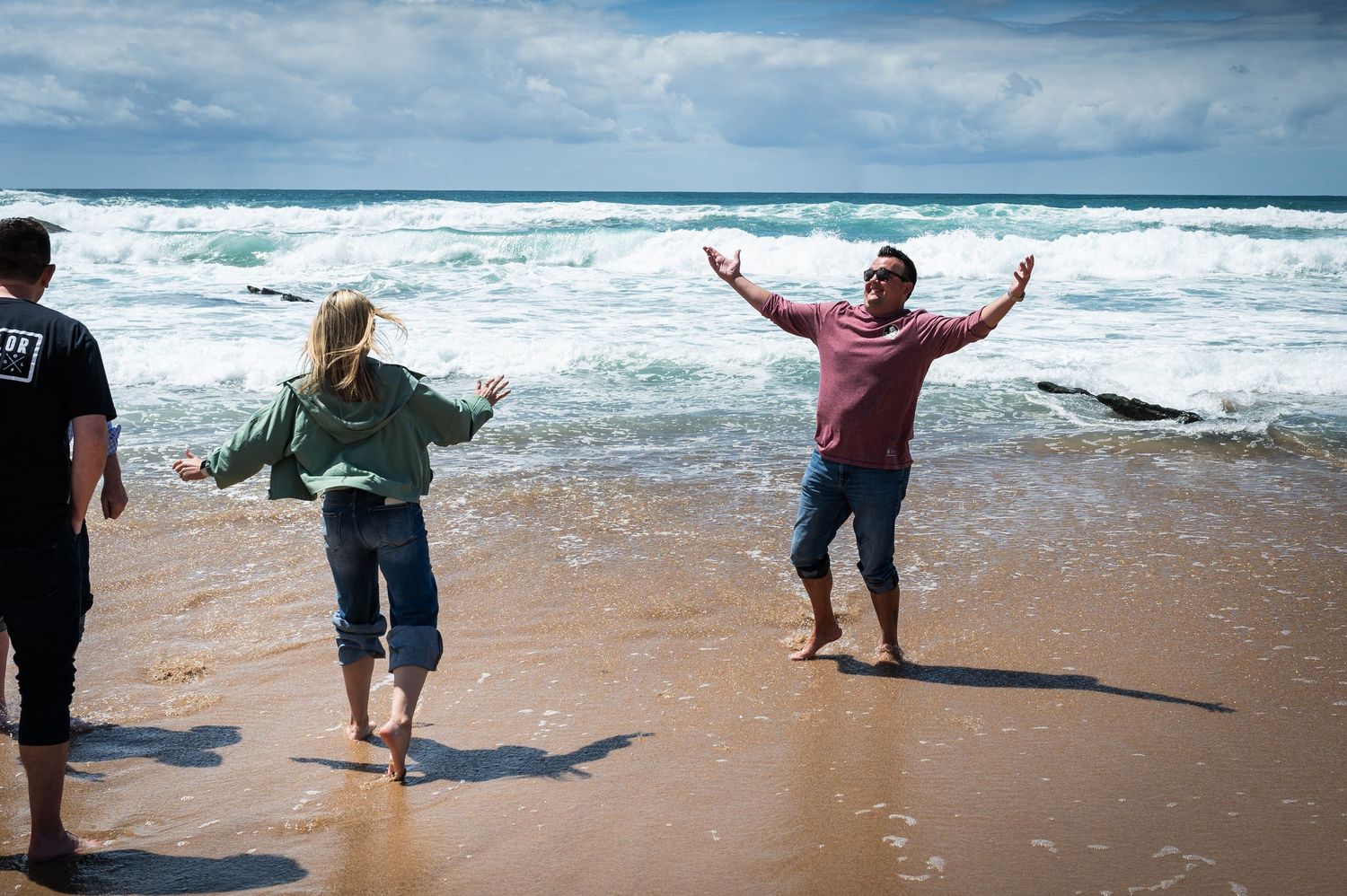 Couple playing joyfully at the edge of ocean waves on a sunny sandy beach.