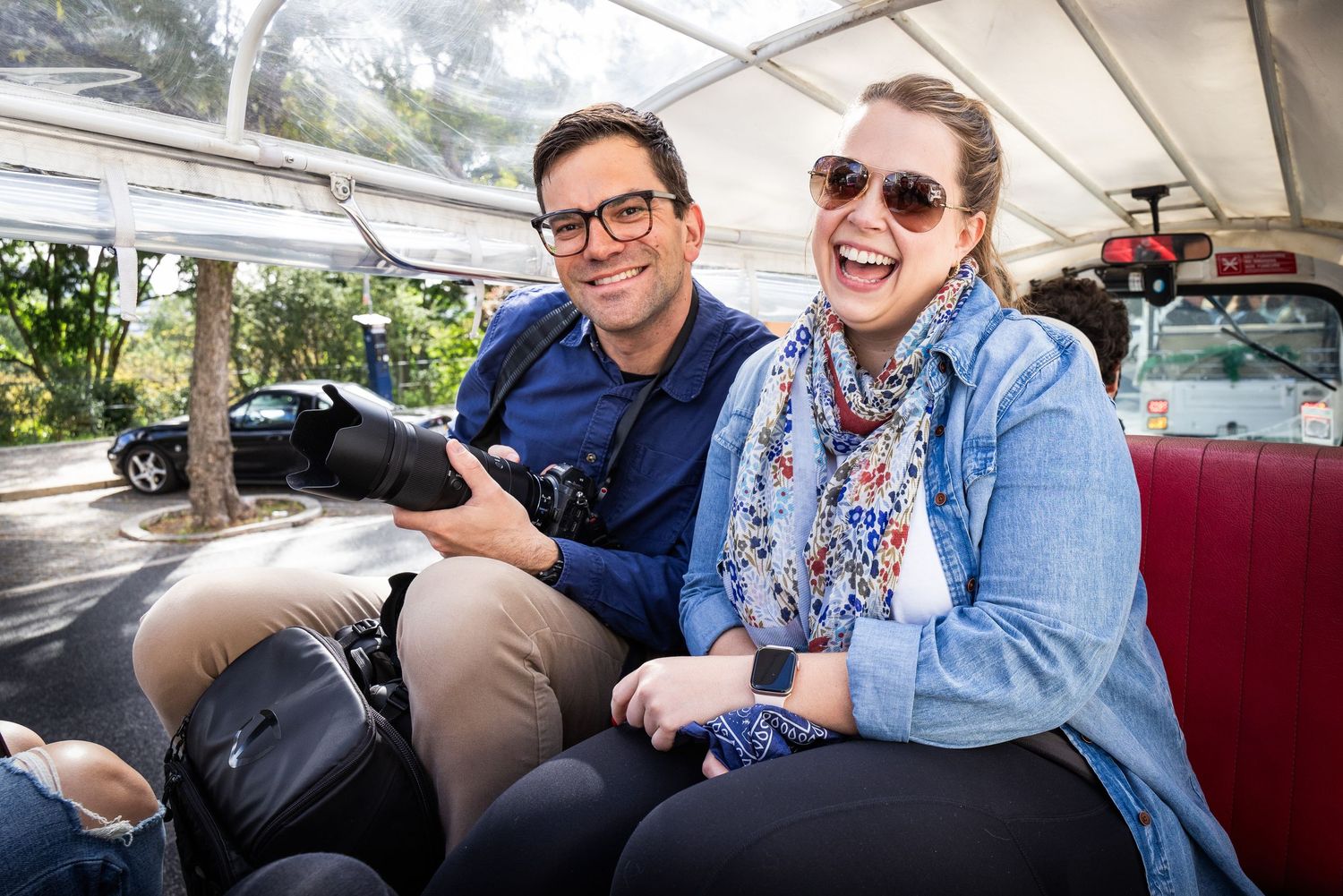 Smiling man and woman riding together on open-air vehicle tour laughing outdoors.
