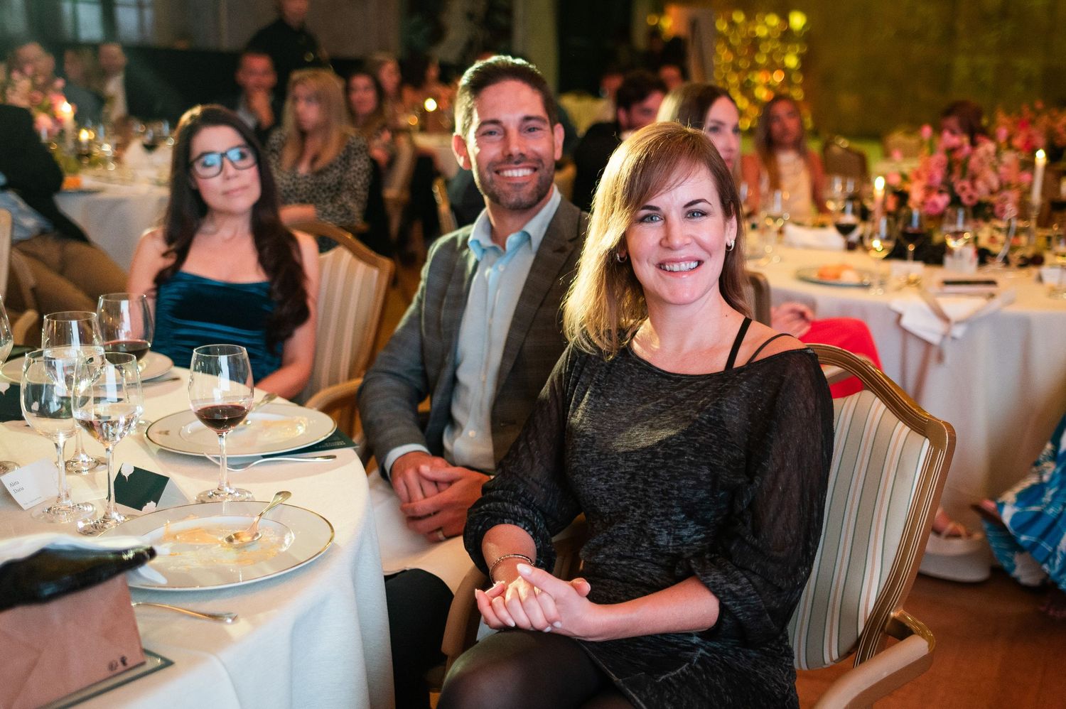 Smiling couple holding hands seated at a candlelit formal dinner gala event.