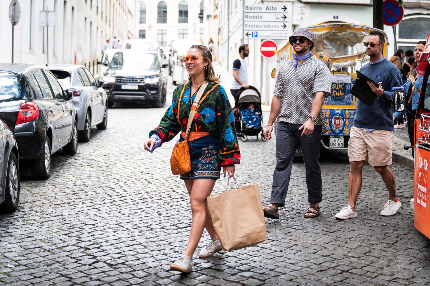 Woman in colorful jacket carrying shopping bags walking on cobblestone city street.