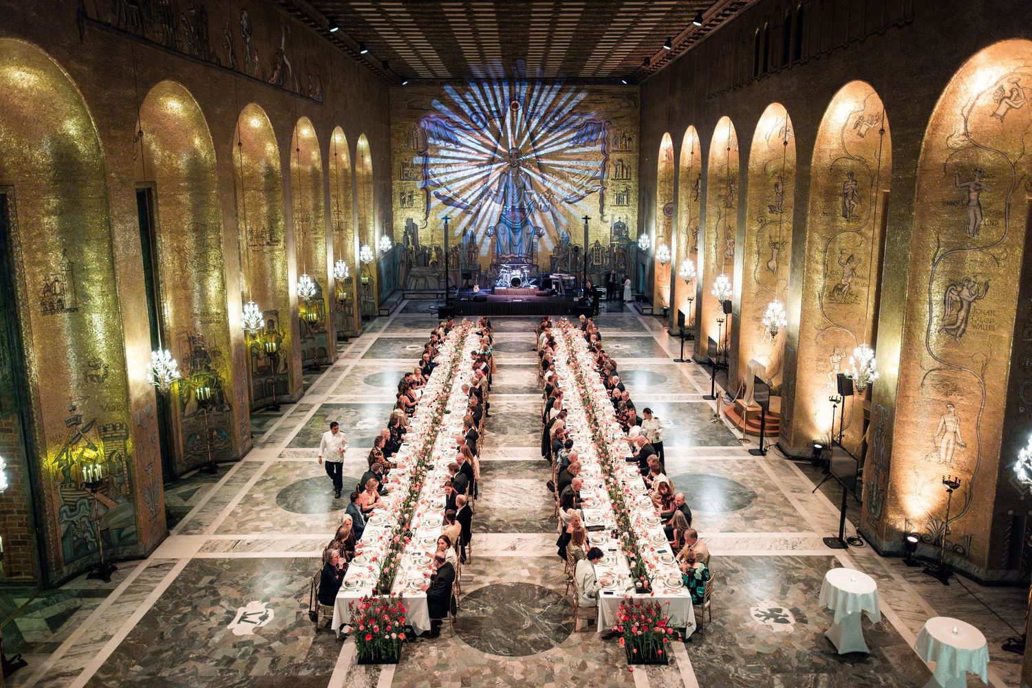 Aerial view of an elegant banquet hall with long dining tables set for a formal event beneath ornate arched ceilings.