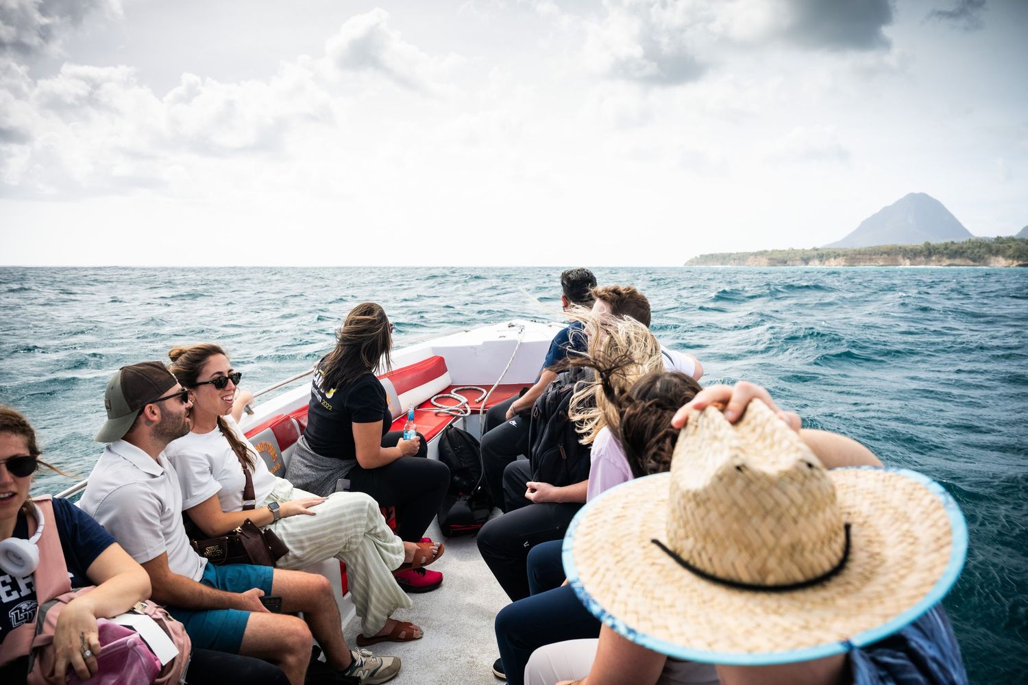 Group of people seated on a boat ride across open blue ocean waters under a cloudy sky.